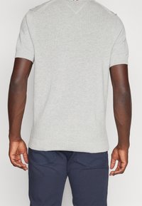 Ljust grå kortärmad stickad tröja med en texturerad yta. Ribbad muddar och nederkant, med en subtil V-ringning på baksidan.