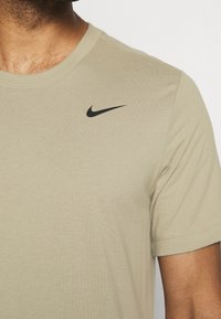 Camiseta de manga corta color mostaza, hecha de algodón. Presenta un logo negro de Nike en la parte superior izquierda del pecho. Textura suave con diseño de cuello redondo.