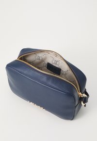 Borsa cosmetica in pelle blu navy con zip dorata, esterno testurizzato e interno a motivo crema con logo. Vista dall'alto aperta.