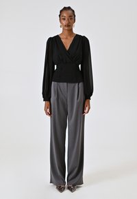 Blusa nera avvolgente con maniche a sbuffo, abbinata a pantaloni larghi grigi. La blusa presenta una vita aderente con bottoni. Tessuti moderni e testurizzati.