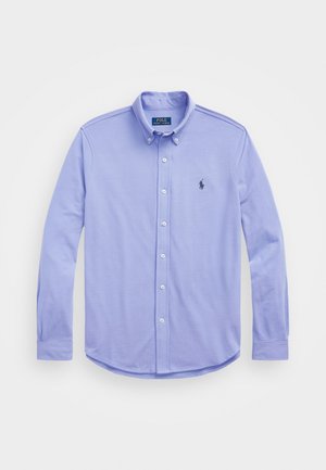 Chemise bleu clair à manches longues avec col boutonné et petit logo foncé sur la poitrine gauche.