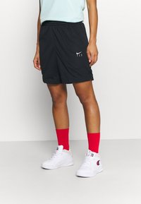 Svarta meshshorts med elastisk midja, prydda med vit "FLY"-logotyp. Matcher med röda strumpor och vita sneakers.