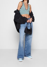 Randig crop-top i teal och svart, oversized svart jacka, utsvängda blå jeans och en liten svart handväska med subtil branding.