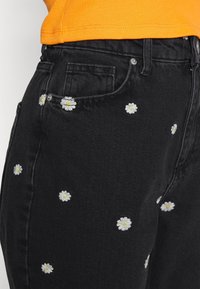 Černé džíny z denimu s rozptýlenou výšivkou bílých a žlutých sedmikrásek, slim fit se přední kapsou a zipovým uzavřením.