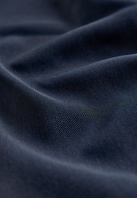 Tissu bleu marine foncé avec une surface lisse et légèrement texturée. Le matériau présente de subtiles ondulations et plis, témoignant de sa flexibilité.