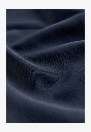 Donker marineblauwe stof met een glad, licht getextureerd oppervlak. Het materiaal vertoont subtiele spanning in rimpels en plooien, wat flexibiliteit aangeeft.