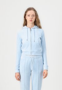 Lichtblauwe, cropped hoodie met verstelbare trekkoorden, voorzakken en subtiele logo. Gecombineerd met bijpassende joggingbroek, met een trekkoord in de taille.