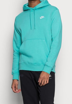 Mężczyzna w turkusowej bluzie z kapturem Nike z przednią kieszenią i czarnych spodniach dresowych Nike Air na jednolitym białym tle.