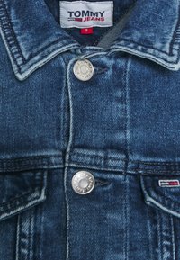 Jeansjacka i mörkblå, med silverfärgade metalld knappar, en spetsig krage och logotypetikett på bröstfickan. Storlek S.