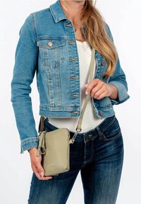 Pieni tekokuitupintainen vihreä olkalaukku vetoketjulla, säädettävällä hihnalla ja hopeisilla yksityiskohdilla; käytössä farkkutakin ja sinisten farkkujen kanssa.