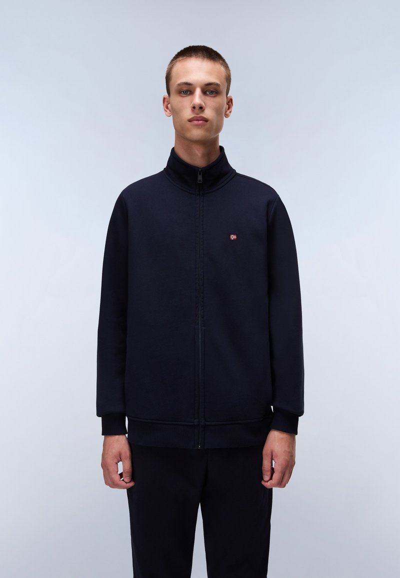 Navy zip-up jacket with high collar and elastic cuffs. Features a small logo on the chest. Smooth fabric with a relaxed fit.