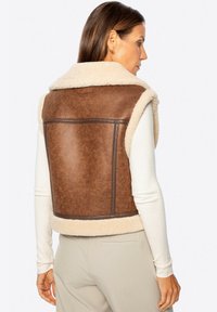 Chaleco de imitación cuero marrón con forro de felpa crema, con cuello y costuras laterales. La parte trasera es lisa y tiene un diseño rectangular.