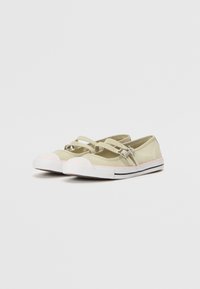 Zapatillas de lona verde claro con correas cruzadas, punteras de goma blanca, acentos rosas en la suela y una base a rayas en blanco y negro.