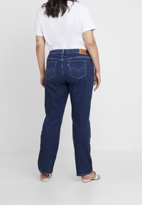 Tummansiniset farkut suoran lahkeen leikkauksella, joissa on nahkainen merkki takana ja kaksi takataskua erottuvalla ompelulla.