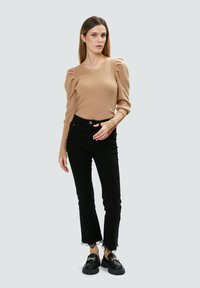 Beige geripptes Langarmoberteil mit puffigen Ärmeln, kombiniert mit schwarzen High-Waist-Jeans mit Spitzenbesatz an den Bündchen und schwarzen klobigen Loafers.