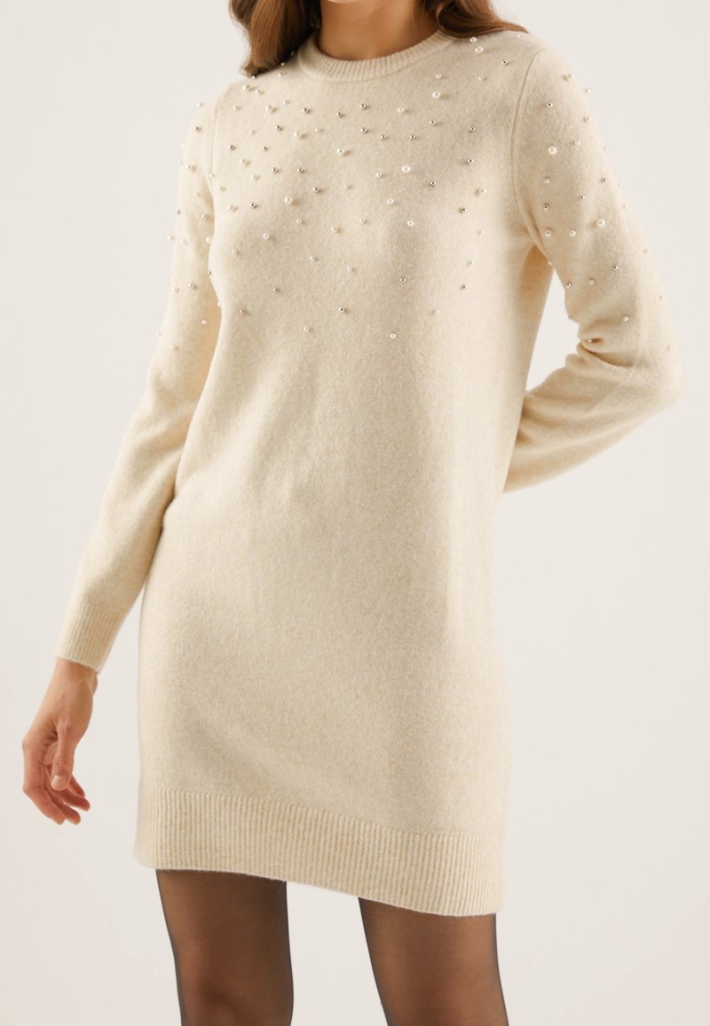 Robe pull beige en tissu doux, ornée de perles décoratives sur le devant, avec des manches longues et un ourlet côtelé.