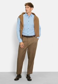 Light blue button-up shirt with small dark dots, brown sweater draped over shoulders, tan trousers, and dark shoes. Simple and clean design.