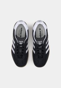 Černé boty Adidas s bílým designem tří pruhů, texturovaným semišovým materiálem, kulatou špičkou a gumovou podrážkou. Mají uzavření na tkaničky.