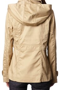 Veste beige à capuche avec taille ajustée et coutures surpiquées, portée par une personne vue de dos, associée à un jean sombre.