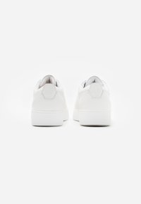 White sneakers with a smooth leather upper, rounded toe, low-top design, and flat rubber soles. Minimalist style with subtle branding on heel.