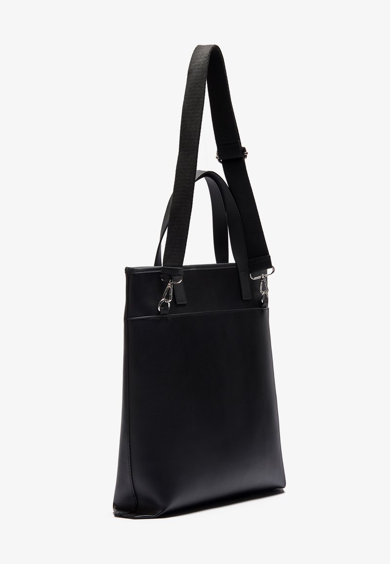 Sac fourre-tout en cuir noir avec une texture lisse, bandoulière en tissu réglable et quincaillerie en argent. Dispose d'une poche avant et d'un design minimaliste.