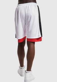 Witte basketbal shorts met een rood en zwart zijstreep, elastische tailleband en een lichtgewicht meshtextuur. Draagt met witte high-top sneakers.