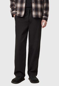 Pantalons noirs tissés avec une coupe décontractée, dotés d'une taille à cordon de serrage et de poches latérales, associés à une chemise à carreaux et des sandales noires.