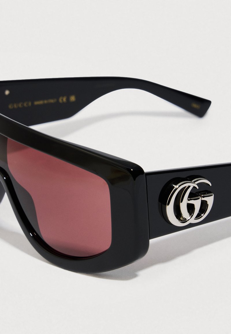 Black acetate sunglasses with pink lenses, thick frames, and a silver double-G logo accent on the temple. Smooth texture throughout.