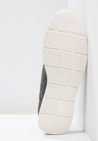 Baskets grises avec un dessus texturé, présentant des motifs découpés. La semelle en caoutchouc blanc plat possède un design de semelle géométrique pour une meilleure traction.