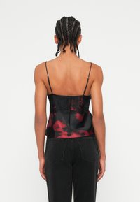 Il top in satin presenta motivi tie-dye neri e rossi, spalline regolabili e un pannello di pizzo sul retro.
