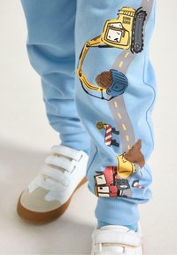 Lichtblauwe joggingbroek met kleurrijke constructiethema-illustraties, waaronder voertuigen en wegdetails, gemaakt van zacht katoenmateriaal.