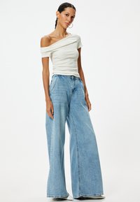 Witte, off-the-shoulder, geribbelde top gecombineerd met lichtblauwe, wijde jeans. De jeans hebben een hoge taille en een subtiele vervaging overal.
