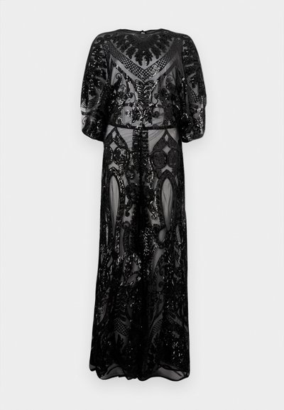 Fekete áttetsző ruha bonyolult gyöngyözött mintákkal, fodros ujjakkal és padlóig érő szegéllyel, egyszerű világos háttér előtt.