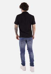 Camicia nera a maniche corte con colletto, abbinata a jeans azzurri chiari. La camicia presenta una trama liscia, mentre i jeans hanno una finitura sbiadita.