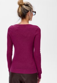 Dopasowany sweter z długim rękawem w intensywnym magencie, o prążkowanej fakturze i okrągłym dekolcie. Prosty fason bez widocznych wzorów czy akcentów.