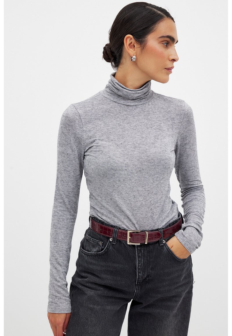 Grauer langärmeliger Rollkragenpullover aus weichem Stoff, kombiniert mit hoch taillierten schwarzen Jeans und einem dunkelroten texturierten Gürtel mit einer Metallschnalle.