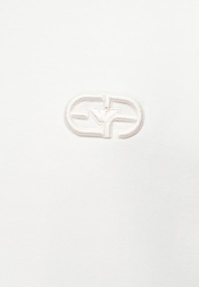 Λευκό ύφασμα με ανάγλυφο κεντητό λογότυπο που διαθέτει διαπλεκόμενα στρογγυλεμένα σχήματα και στυλιζαρισμένα γράμματα σε λευκό νήμα που ταιριάζει.