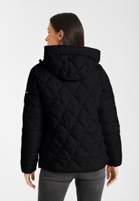 Zwarte gewatteerde pufferjack met een capuchon, een gestructureerd diagonaal patroon en een logo-detail aan de zijkant, met lange mouwen en een getailleerd silhouet.