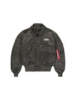 Chaqueta de vuelo en nylon verde oscuro con cuello y puños acanalados, cierre de cremallera al frente, dos bolsillos frontales y una etiqueta roja en la manga izquierda.