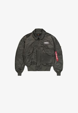 Veste de vol en nylon vert foncé avec un col et des poignets côtelés, fermeture éclair à l'avant, deux poches avant et une étiquette rouge sur la manche gauche.