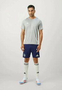 Grå treningst-skjorte, marineblå shorts med logo, hvite strømper til kneet med svarte striper, og blå fotballsko. Enkel design, lett stoff.