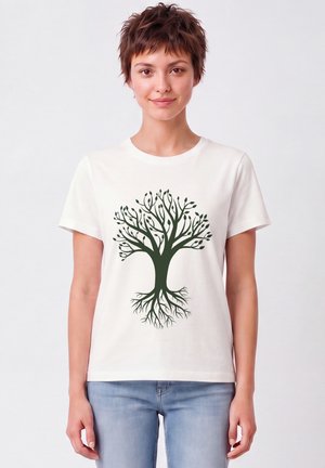 Junge Frau mit kurzen Haaren, die ein weißes T-Shirt mit einer grünen Baumgrafik trägt, die Äste und Wurzeln zeigt, kombiniert mit hellblauen Jeans.