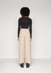 Top noir à manches longues et pantalon beige à jambes larges, avec une texture lisse et des poches arrière discrètes, associés à des bottines.