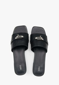 Zwarte leren slip-on sandalen met een vierkante teen, een brede band met zilverkleurige hardware, en een gladde, platte zool. Merklogo zichtbaar.