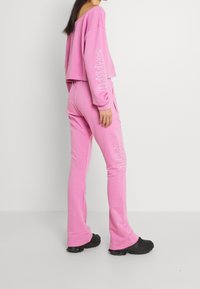 Roze cropped sweatshirt met een off-shoulder ontwerp. Bijpassende roze joggers hebben een witte logo langs het been. Zwarte chunky schoenen maken de look compleet.