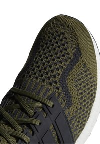 Gros plan sur une chaussure de sport tricotée verte et noire avec des lacets verts et une semelle blanche.