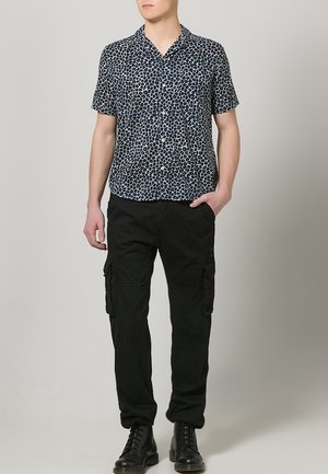 Koszula z krótkim rękawem w kolorze granatowym z wzorem w panterkę, zestawiona z czarnymi spodniami cargo z bocznymi kieszeniami i czarnymi butami na sznurówki.