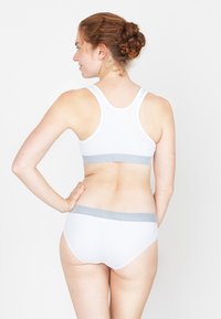 Witte sportbeha met een grijze elastische band, gecombineerd met witte slips met een soortgelijke grijze tailleband. De stof lijkt zacht en rekbaar.