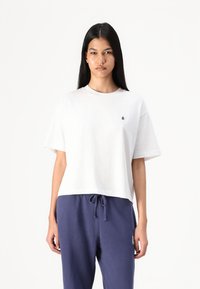 Weißes Baumwoll-T-Shirt mit Rundhalsausschnitt und kurzen Ärmeln. Es verfügt über ein kleines schwarzes Logo auf der linken Brust und hat eine lockere Passform.