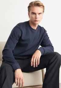 Marinblå sweatshirt i mjukt tyg med rund halsringning, ribbade ärmslut och en subtil logotypdetalj på bröstet. Styler med svarta byxor.